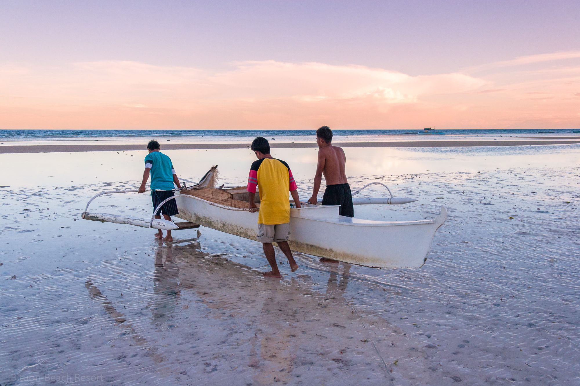 Fischer tragen ein Auslegerboot bei Sonnenuntergang am Strand von Anda – Zwischenstopp der Tour vom Bituon Beach Resort.